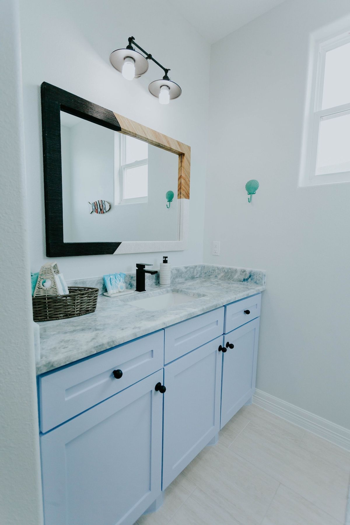 A bathroom vanity with pale blue cabinets, a marble countertop, black hardware, and a two-toned framed mirror.