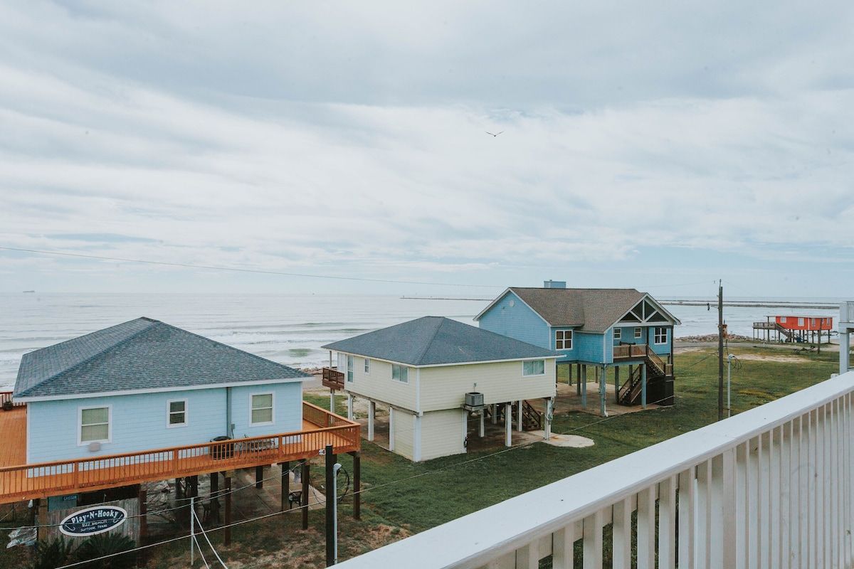 Beachfront stilt houses under a cloudy sky, viewed from an elevated deck.