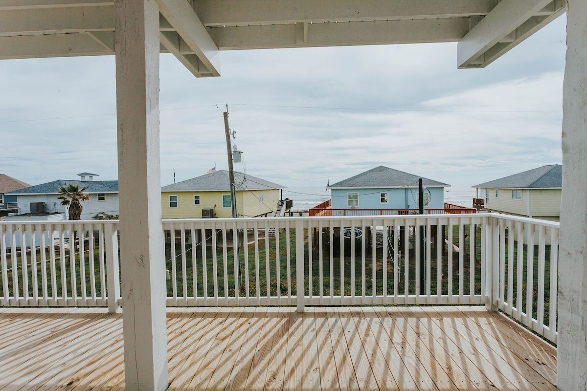 A view from a wooden deck looking out at several pastel-colored beach houses under a cloudy sky.