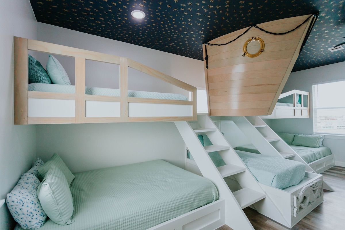 Bunk beds in a room with a ship-themed ceiling and prow feature, featuring a white staircase and mint bedding.