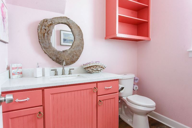 A bathroom with pink cabinets , a toilet , a sink and a mirror.