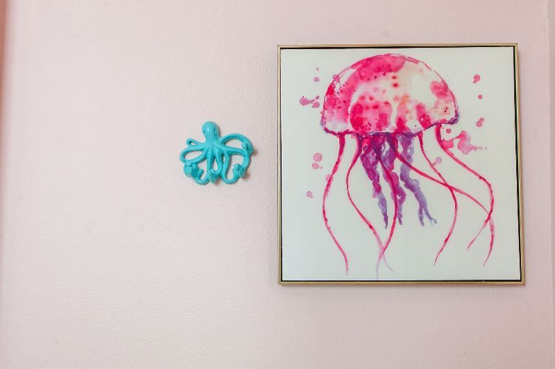 A pink jellyfish is hanging on a pink wall next to a blue octopus.