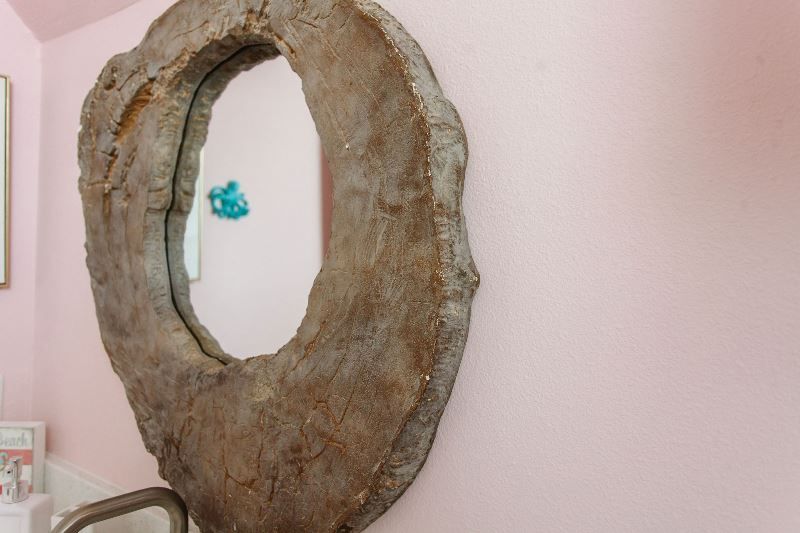 A large round mirror is hanging on a pink wall.