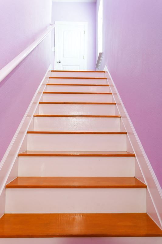 A set of white stairs with wooden steps leading up to a purple wall.