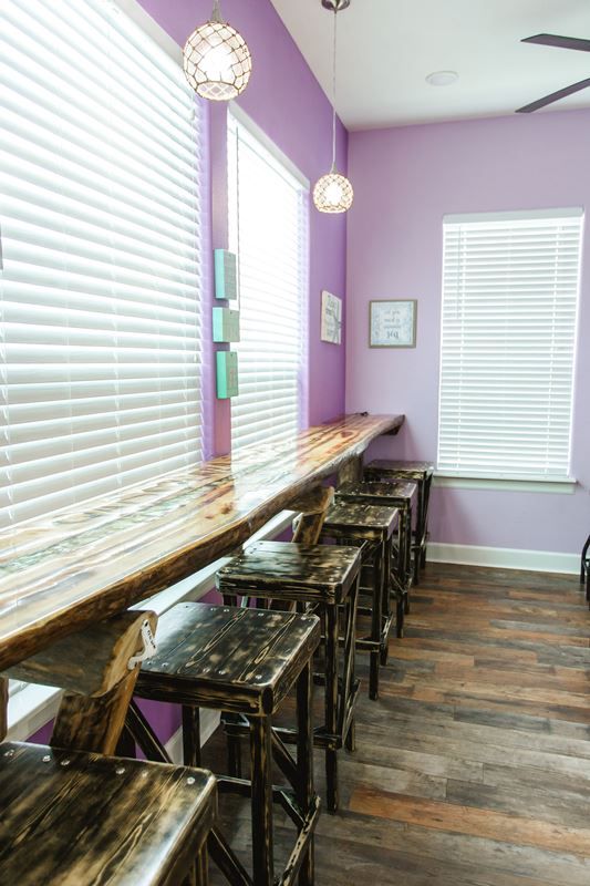 A row of wooden stools are lined up in a room with purple walls.