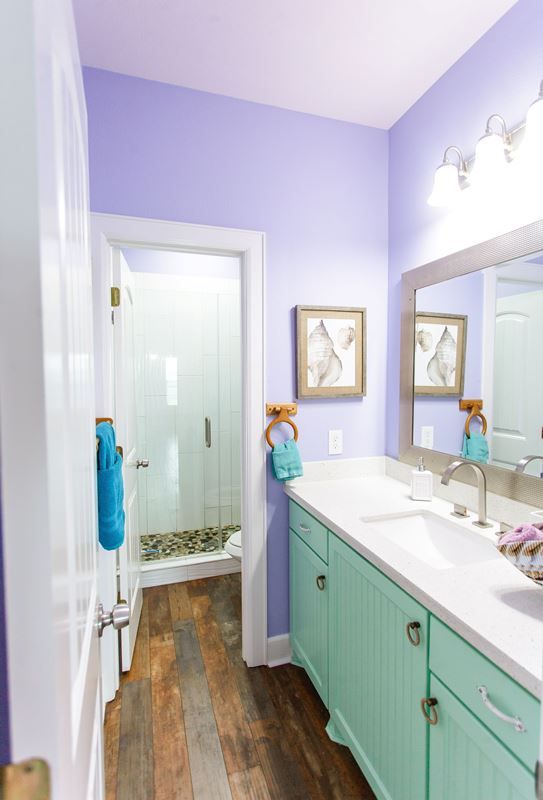 A bathroom with purple walls , blue cabinets , a sink and a mirror.