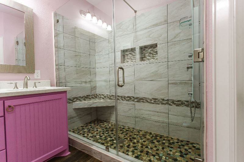A bathroom with a pink vanity and a walk in shower with a glass door.