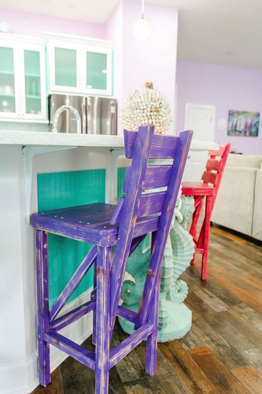 A purple bar stool is sitting next to a seahorse statue in a kitchen.