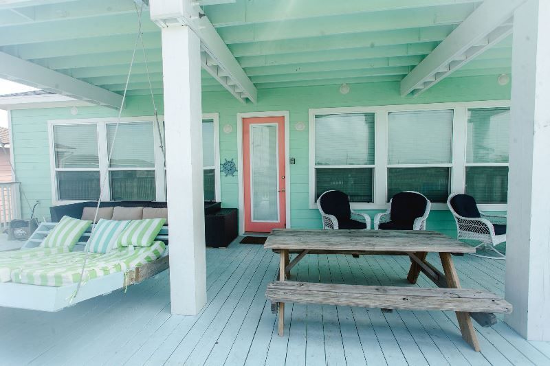 A green house with a picnic table and chairs on the porch.
