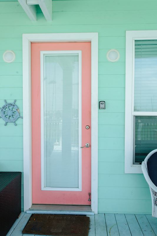 A pink door with a white trim is on a green house.