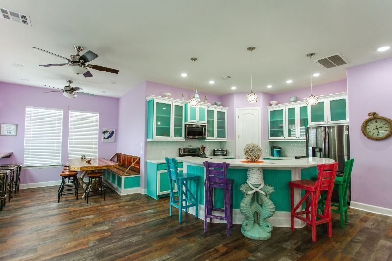A kitchen with purple walls , teal cabinets , purple stools and a clock on the wall.
