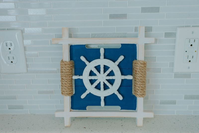 A blue and white steering wheel is hanging on a white tiled wall.