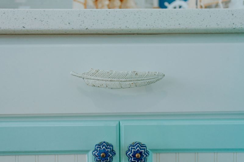 A close up of a feather shaped handle on a cabinet.