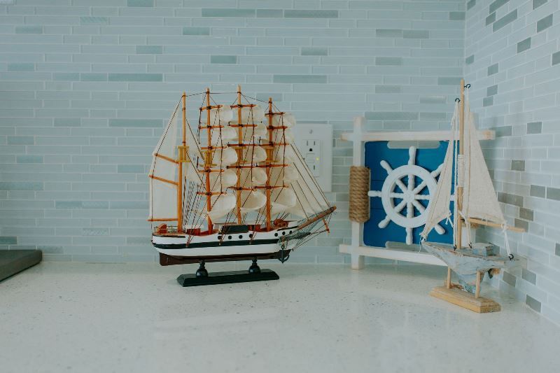 A model sailboat is sitting on a counter next to a picture of a steering wheel.