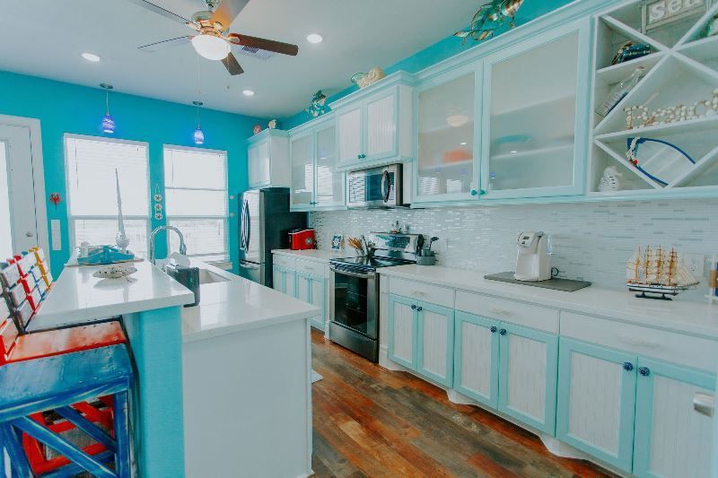 A kitchen with blue walls and white cabinets and a ceiling fan.