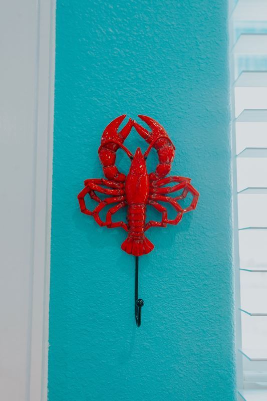A red lobster hook is hanging on a blue wall.