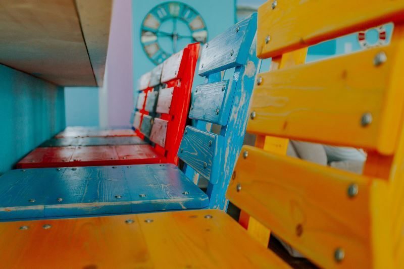 A row of colorful wooden benches with a clock in the background.