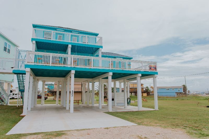 A blue and white house with a large deck is sitting on top of a grass covered field.
