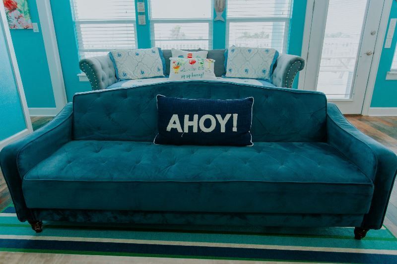 A blue couch with a pillow that says ahoy on it in a living room.