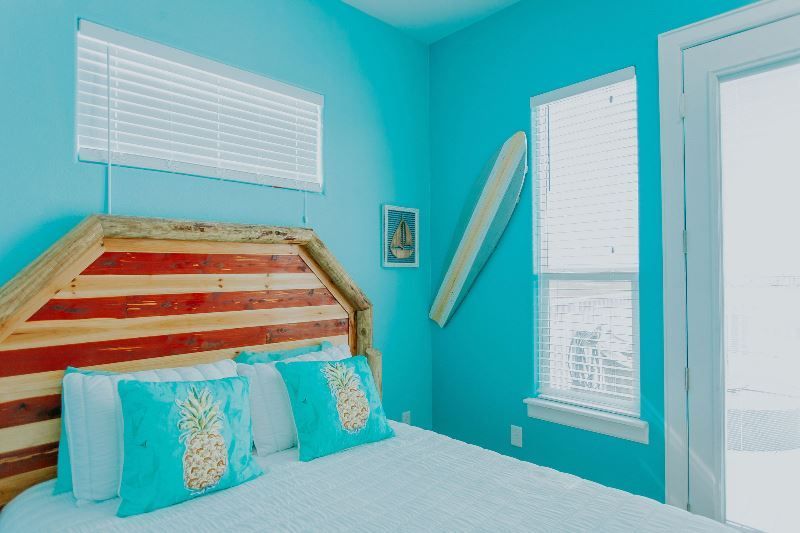 A bedroom with blue walls and a bed with pineapple pillows and a wooden headboard.
