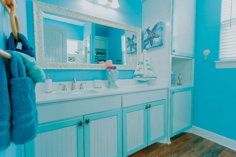 A bathroom with blue walls , white cabinets , a sink and a mirror.
