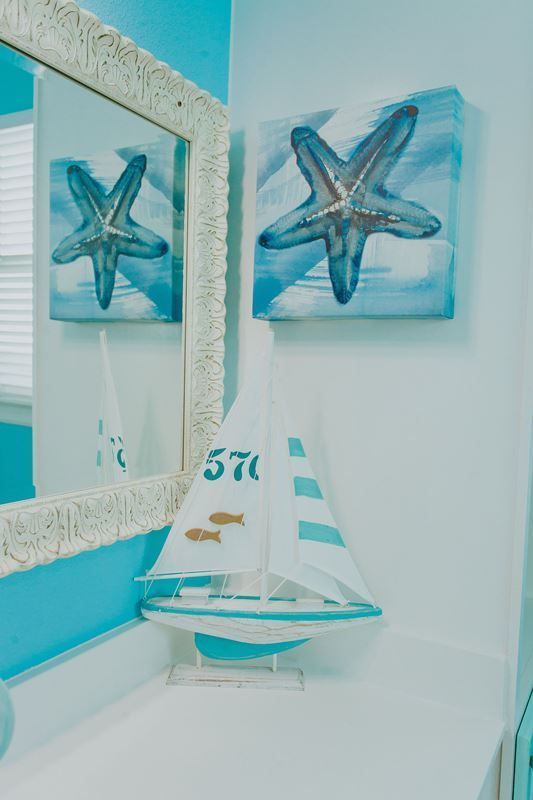 A bathroom with a sailboat and starfish paintings on the wall.