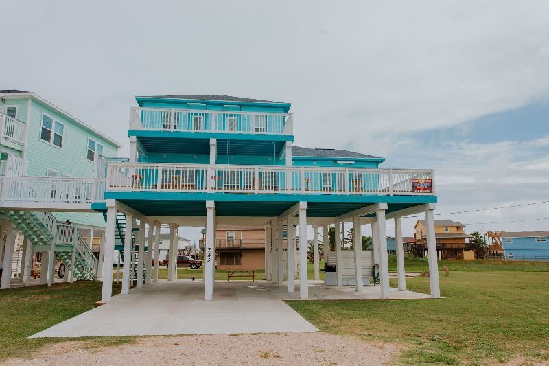 A large blue house on stilts with a large deck.