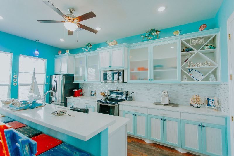 A kitchen with blue cabinets and white counter tops and a ceiling fan.