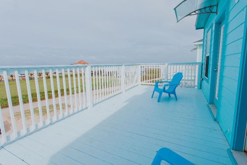 A blue deck with blue chairs and a white railing overlooking the ocean.