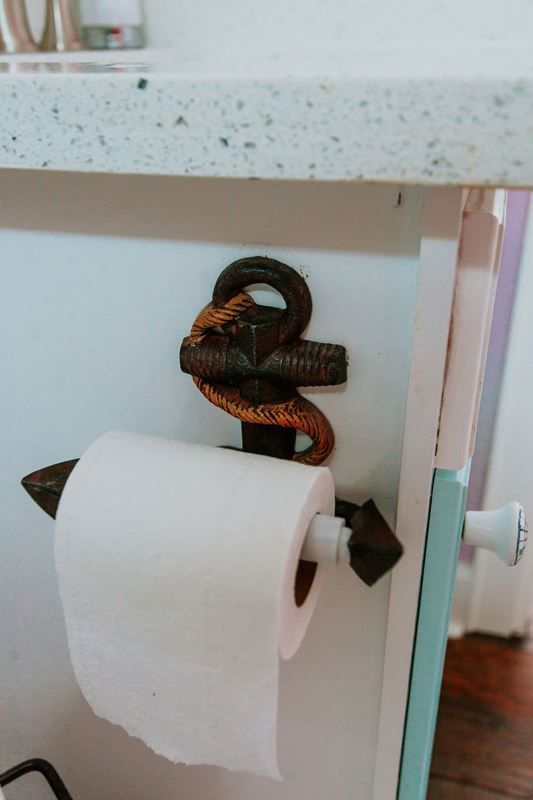 A roll of toilet paper is hanging on a toilet paper holder shaped like an anchor.