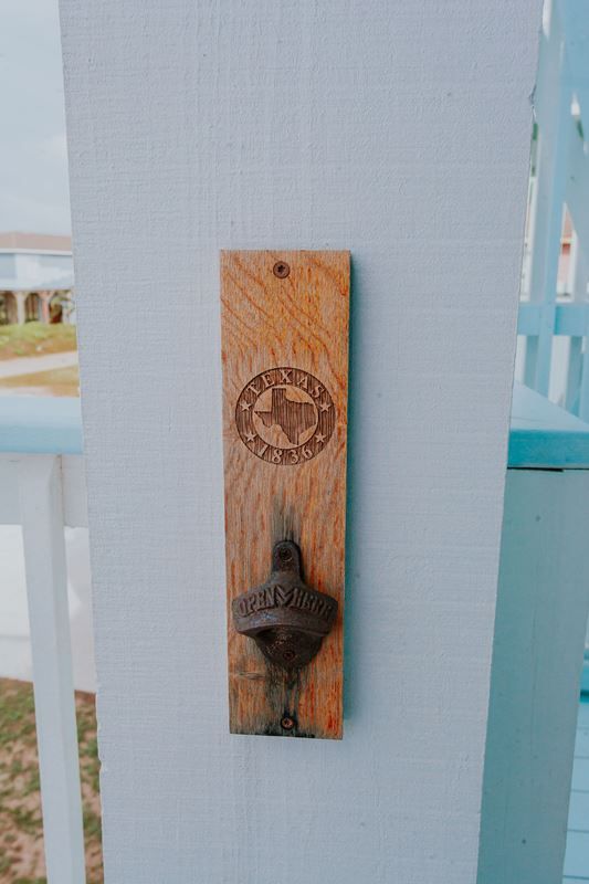 A wooden bottle opener is hanging on a white wall.