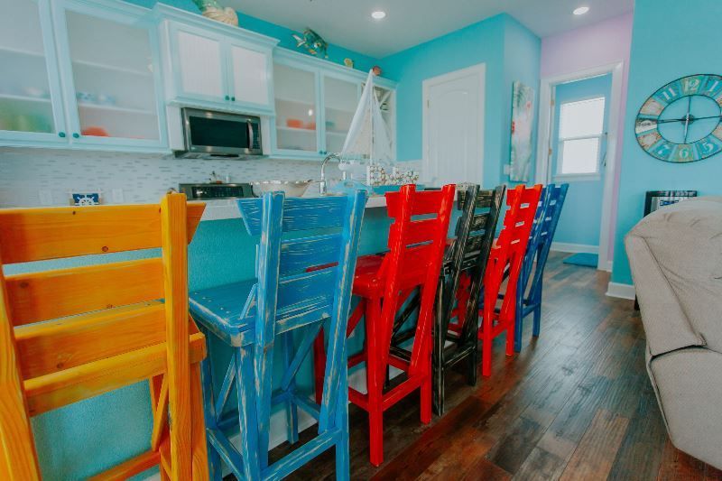 A kitchen with a lot of colorful chairs and a clock on the wall.