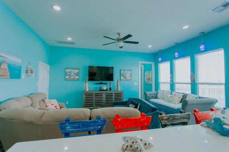 A living room with blue walls , a couch , a television and a ceiling fan.