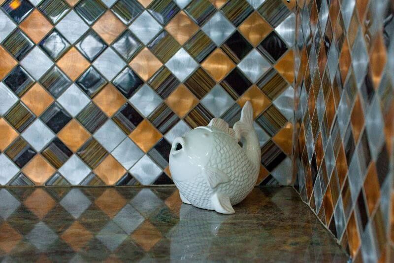 A white teapot is sitting on a counter in front of a checkered tile wall.