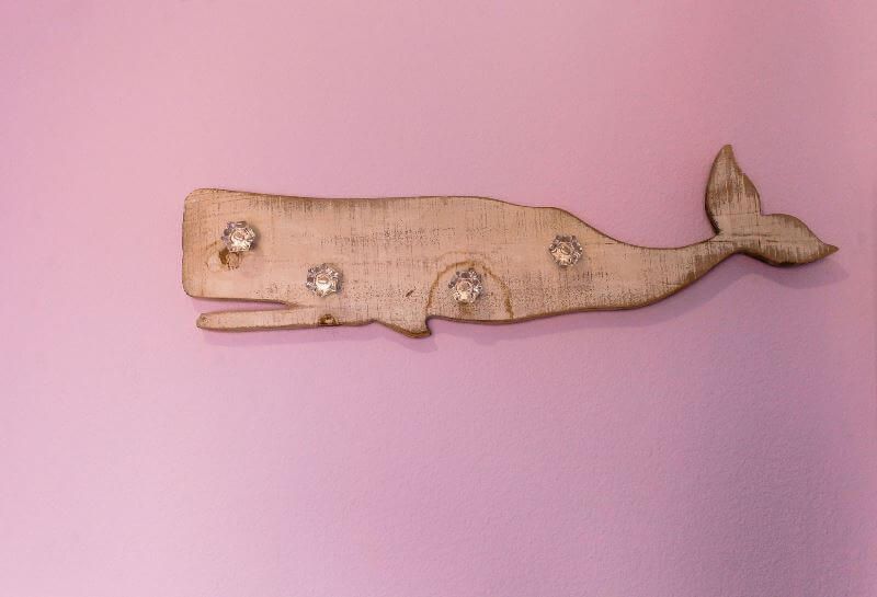 A wooden whale is hanging on a pink wall.