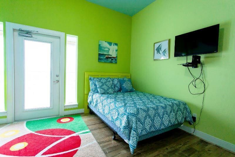 A bedroom with green walls , a bed , a television and a rug.