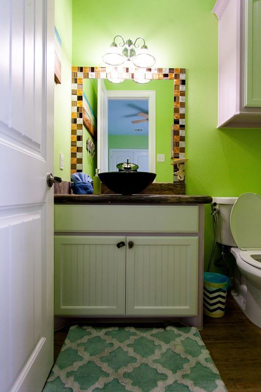 A bathroom with green walls , a sink , a toilet and a mirror.