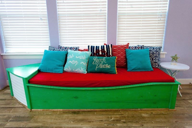 A green couch with red cushions and pillows in a living room.