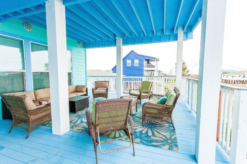 A blue deck with wicker furniture and a blue house in the background.