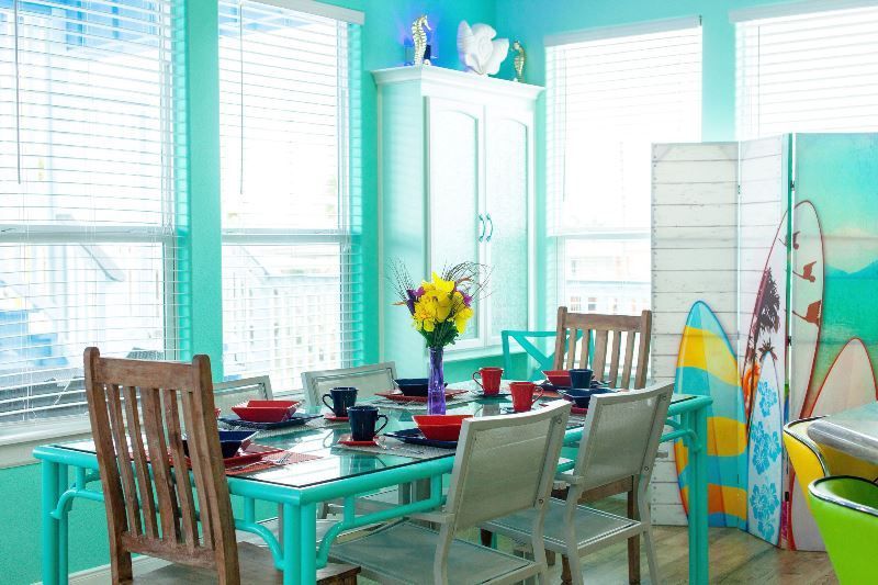 A dining room with a table and chairs and a surfboard on the wall.
