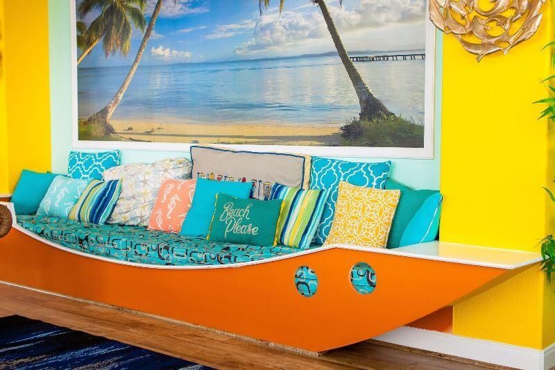A living room with a boat shaped couch and a picture of a beach on the wall.