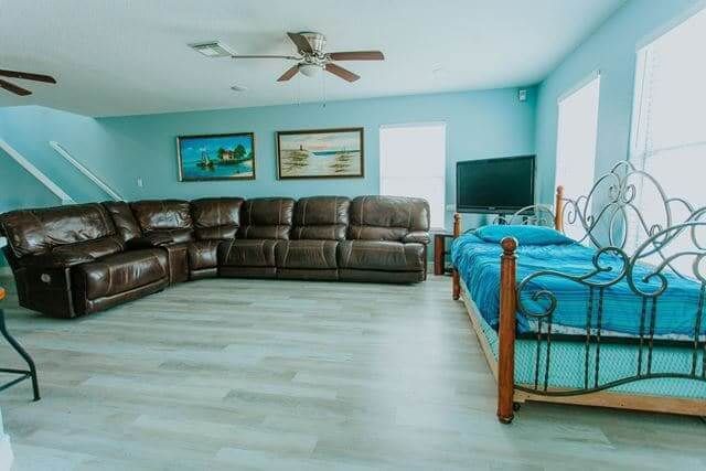 A living room with a couch , bed , television and ceiling fan.
