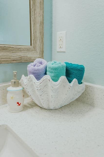 A bathroom sink with a shell filled with towels and a soap dispenser.