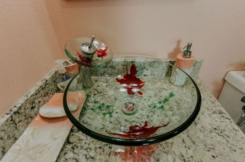 A bathroom sink with a glass bowl on a granite counter top.