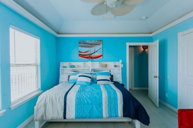 A bedroom with blue walls and a bed and a ceiling fan.