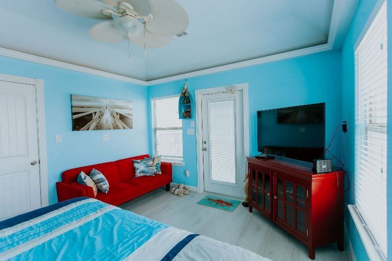 A bedroom with blue walls , a red couch , a television and a ceiling fan.