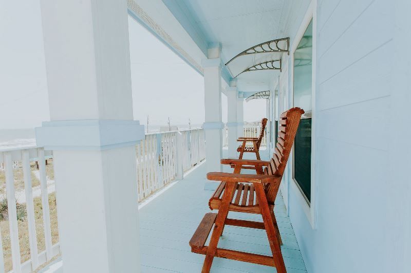 There are two wooden chairs on the porch of a house.