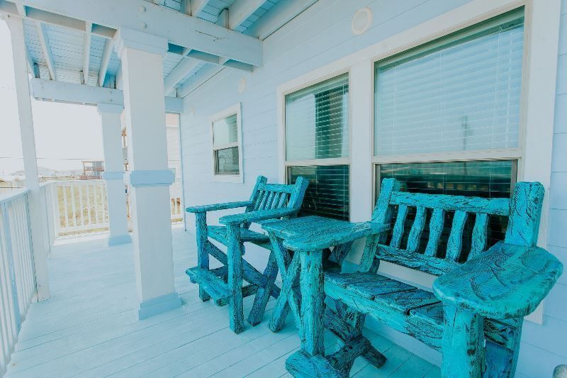 There are two blue chairs on the porch of a house.
