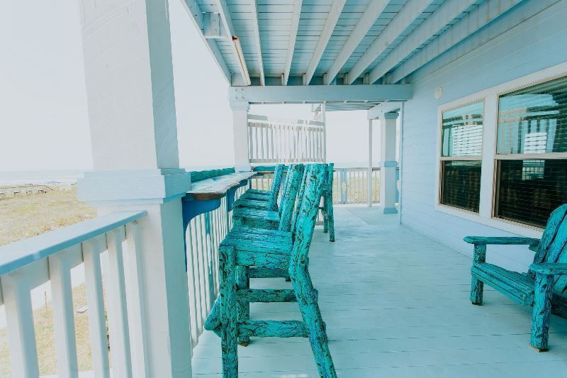 There are a lot of blue chairs on the porch of a house.