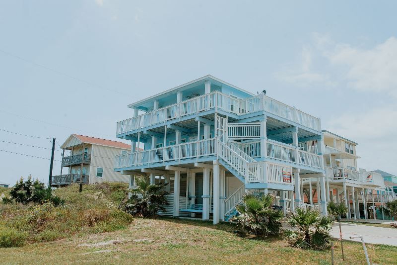 A large blue and white house with stairs leading up to it is sitting on top of a grassy hill.